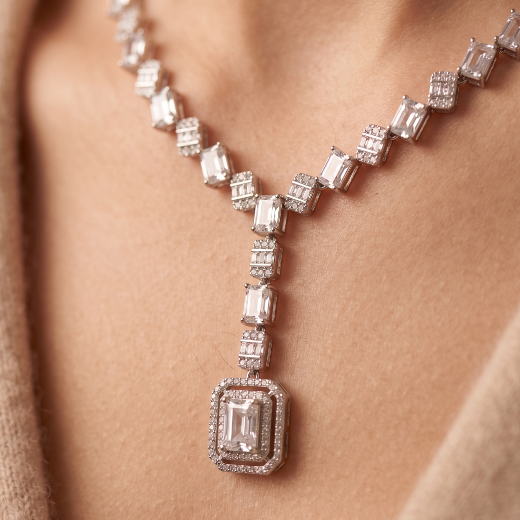 Close-up of emerald and diamond necklace held between fingers, showing vivid green stones set in gold with sparkling details.